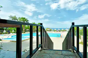 Blick von der Terrasse über einen Steg mit Geländer auf das Schwimmbecken und Liegen mit Sonnenschirmen.