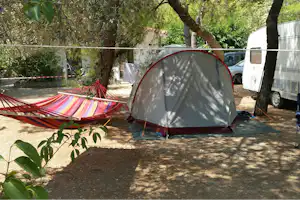 Campingzelt im Schatten unter Bäumen, daneben eine Hängematte und Wohnwagen auf dem Stellplatz.