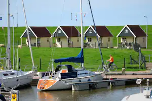 Camping Zeestrand Eems-Dollard - Boote und das Meer im Vordergrund, Mobilheime an einer Weide mit Schafen im Hintergrund