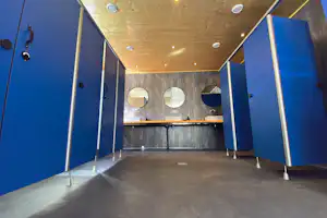 Offener Waschraum im Campingbereich mit mehreren Waschbecken, blauen Trennwänden und beleuchteter Holzdecke.