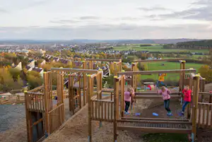 Spielbereich auf einer Holzterrasse mit Rutsche und Sandfläche, Blick über das Tal und Häuser in der Ferne.