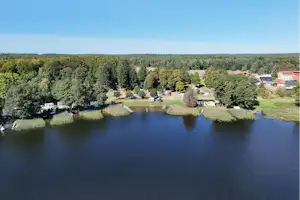 Luftaufnahme eines Campingplatzes am See mit Ufer, Bäumen, Wegen und mehreren Wohnwagen und Gebäuden.
