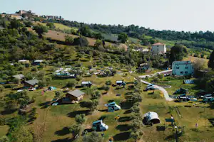Campinganlage in Hanglage mit Wohngebäude, Stellplätzen für Wohnmobile und Zelten sowie vielen Bäumen und Wiesen.