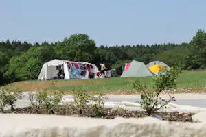 Zelte auf einem Campingplatz mit Wäscheleine, Kiesweg und grünen Bäumen im Hintergrund.