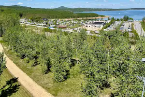 Campingplatz mit vielen Stellplätzen, Wohnmobilen und Bäumen, Blick auf den See und die Uferlinie in der Ferne.