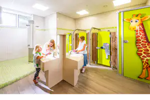 Kinderwaschbecken im hellen Sanitärraum, grüne Türen und ein großes Giraffenbild an der Wand.