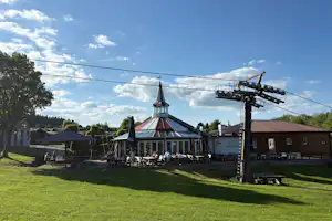 Campingplatz mit Rasenfläche, Pavillon mit Glockenturm und Sitzbereich, daneben ein großer Kran und Wohnwagen am Rand.