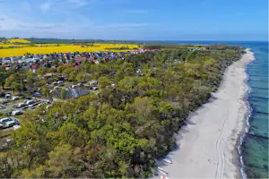 Campingplatz mit Wohnwagen und Stellplätzen am Strand, Blick über die Küste mit Bäumen und Häusern im Hintergrund.