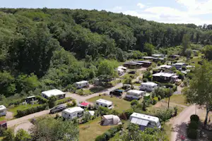 Campingplatz mit Wohnmobilen und Zelt auf einer Wiese, umgeben von Bäumen und Wegen im Grünen.