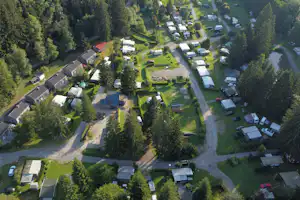 Luftaufnahme einer Campinganlage mit Wohnwagen, Stellplätzen, Wegen und mehreren Gebäuden inmitten von Bäumen und Grünflächen.