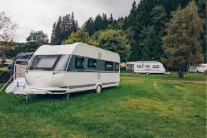 Zwei Wohnwagen auf einem Campingplatz auf grünem Gras, mit Vorzelten und Bäumen im Hintergrund.