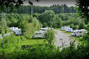 Wohnmobile auf einem Campingplatz im Grünen, mit Rasenflächen, Hecken und einem Weg zwischen den Stellplätzen.