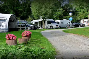 Campingplatz mit Stellplätzen für Wohnmobile und Autos, Kiesweg, Zelt am Rand und Bäume im Hintergrund.
