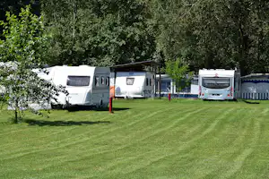 Wohnmobile auf einem grünen Campingplatz, Rasenfläche mit Stellplätzen und Bäumen im Hintergrund.