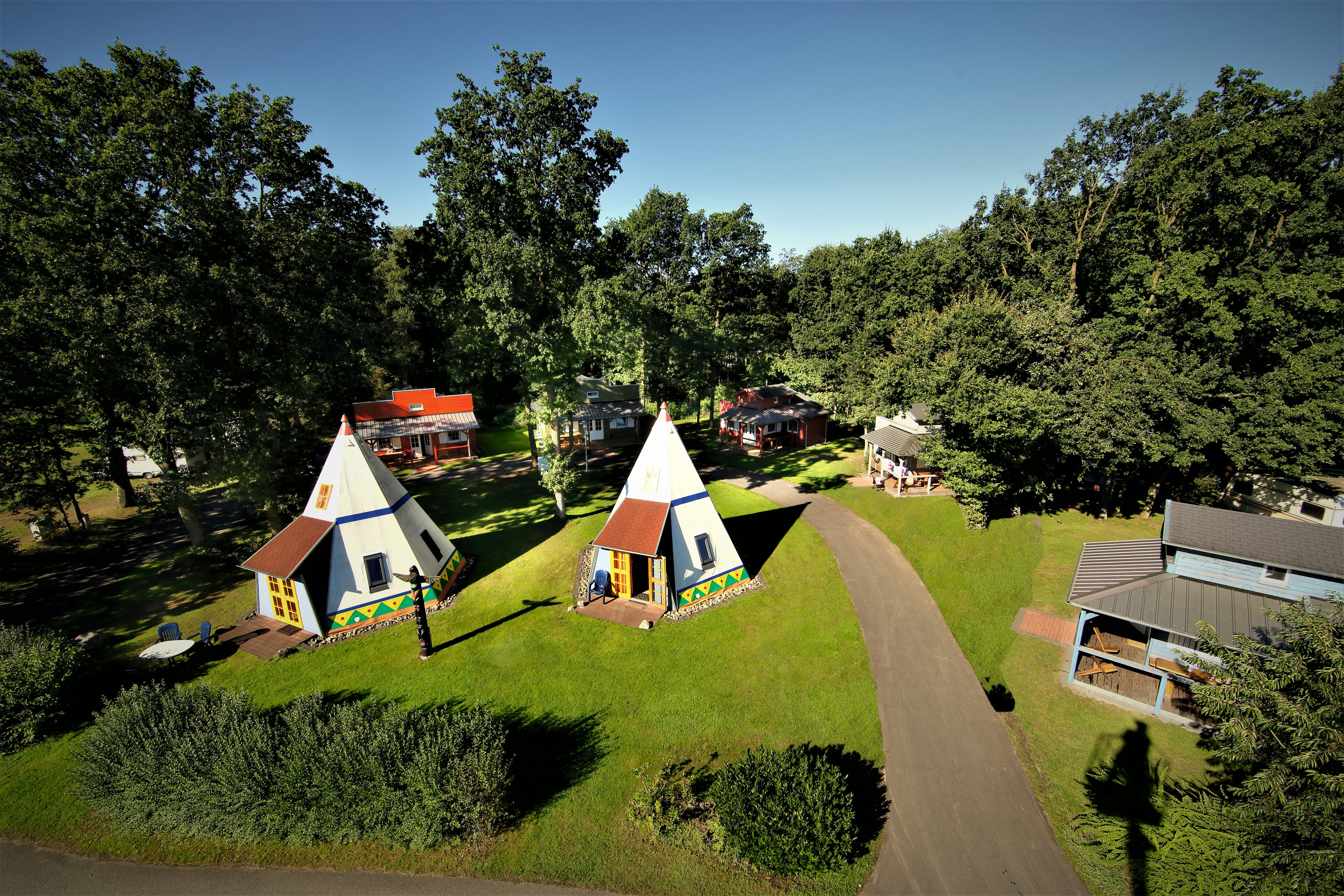 Zwei Zelte auf einem Campingplatz mit Rasenwegen, Bäumen und weiteren Stellplätzen im Hintergrund.