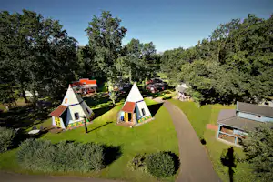 Zwei Zelte auf einem Campingplatz mit Rasenwegen, Bäumen und weiteren Stellplätzen im Hintergrund.