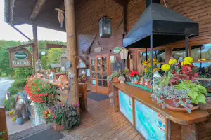 Holzveranda mit Blumenampeln, Laterne und Sitzbereich, Holzwand und Fensterfront am Campinggebäude.