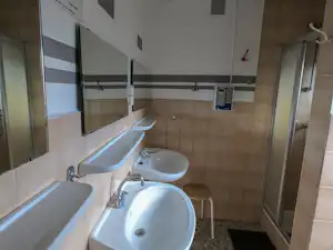 Badezimmer mit zwei Waschbecken, Spiegeln und Dusche, hell geflieste Wände und Tür im Hintergrund.