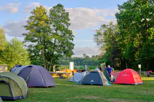 Zeltplatz mit mehreren Zelten auf einer Wiese, Bäume im Hintergrund und ein Weg zwischen den Stellplätzen.