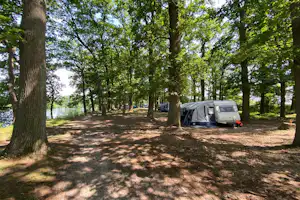 Zelt auf einem Stellplatz im Wald, zwischen Bäumen, mit Blick auf einen See und einem geparkten Auto.
