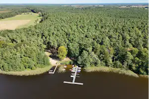 Holzstege im Fluss vor einem Waldgebiet, daneben Wiesen und ein kleiner Weg am Ufer.