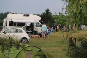Wohnmobil auf dem Stellplatz, davor ein Auto und eine Familie mit Hund auf dem grünen Campinggelände.