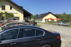 Campinggebäude mit Beschilderung „Leibnizstübchen“, Parkplatz mit Autos und orangefarbenen Sonnenschirmen vor dem Eingang.