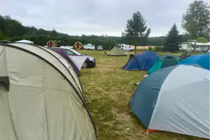 Zelte auf einem Campingplatz auf einer Wiese, daneben geparkte Autos und weitere Zelte im Hintergrund.
