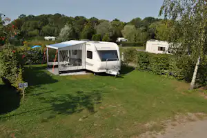 Wohnmobil mit Vorzelt auf einem grünen Campingplatz, umgeben von Bäumen und Hecken, mit Stellplatzfläche aus Gras.