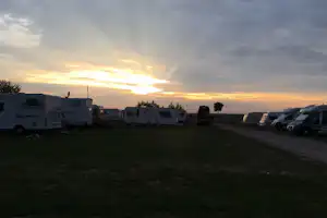 Wohnwagen und Autos auf einem Campingplatz, Blick auf die Reihe der Stellplaetze bei Sonnenuntergang am Himmel.