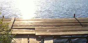 Holzsteg am See mit Wasser und Wellen, im Vordergrund Schilf und Holzplanken.