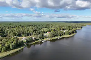 Luftaufnahme eines Flusses mit Uferwegen, Bootsstegen und Campingplätzen im Grünen, umgeben von Wald und Wolken am Himmel.