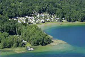 Luftaufnahme eines Campingplatzes am See mit Stellplätzen, Wohnwagen und Bootsstegen im grünen Wald.