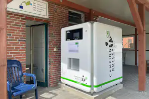 Servicebox für Wohnmobil auf dem Campingplatz vor Backsteinwand und Eingangstür, mit Sitzbank und Schild an der Wand.