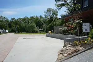 Betonweg und Terrasse am Campingplatz, mit Blumenbeeten, Steinkante und Bäumen im Hintergrund.