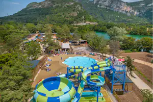 Großes Freibad mit blauen Rutschen und Planschbecken, Campingplatz mit Stellplätzen und Wegen, umgeben von grünen Hügeln.