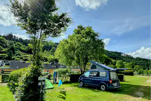 Wohnmobil und Zelt auf einem grünen Campingplatz, Hecken und Bäume, daneben ein Parkplatz mit Wohnmobil.