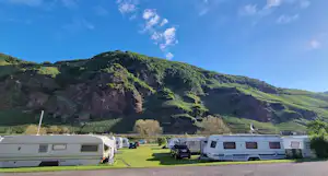 Wohnwagen auf einem grünen Campingplatz am Hang, mit weiteren Stellplätzen und Blick auf das Tal und die Hügel.