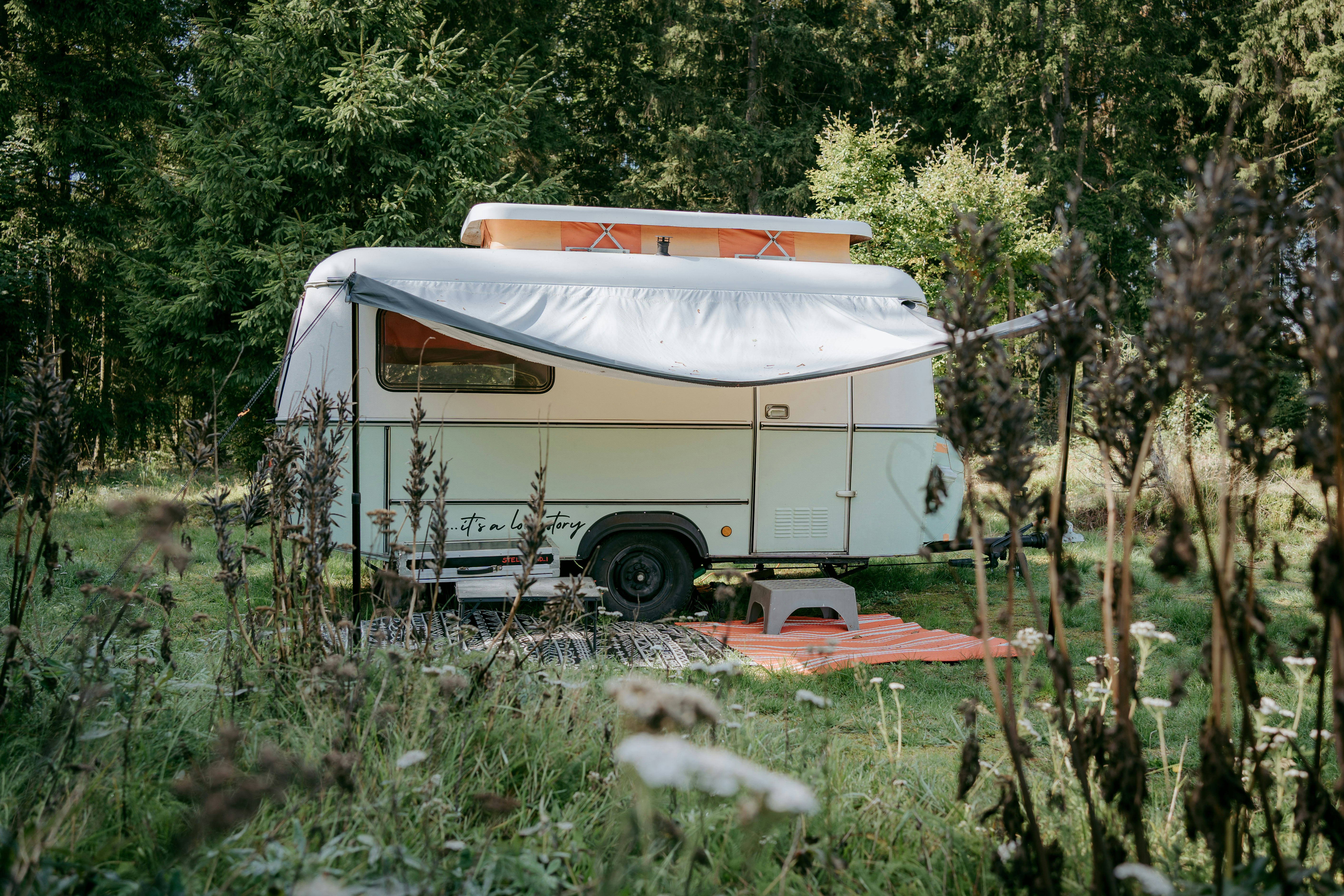 Wohnmobil mit Markise auf einem Campingplatz im Grünen, umgeben von Bäumen und Gras.