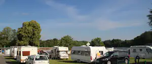 Reihe von Wohnmobilen und Caravans auf einem Campingplatz, mit Autos davor und Bäumen im Hintergrund.