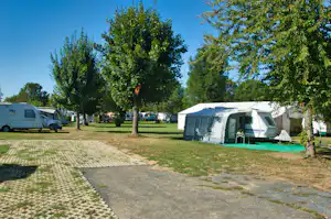 Wohnwagen und Zelte auf einem Campingplatz, gepflasterter Weg und Rasen zwischen Bäumen, Wohnmobilen am Rand.