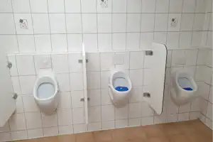 Drei Toiletten in einer Sanitäranlage mit weißen Keramikschalen, Fliesenwänden und braunem Boden.