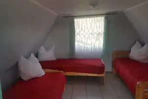 Drei Betten in einem Zeltzimmer mit roten Decken, weißen Kissen, Vorhangfenster und grauem Fliesenboden.