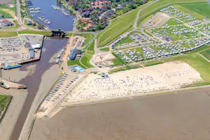 Luftaufnahme eines Campingplatzes am Fluss mit Stellplätzen, Wegen und Booten im Hafenbereich.