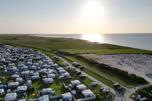 Campingplatz an der Küste mit Wohnwagen und Stellplätzen, Weg zum Strand und Blick aufs Meer.