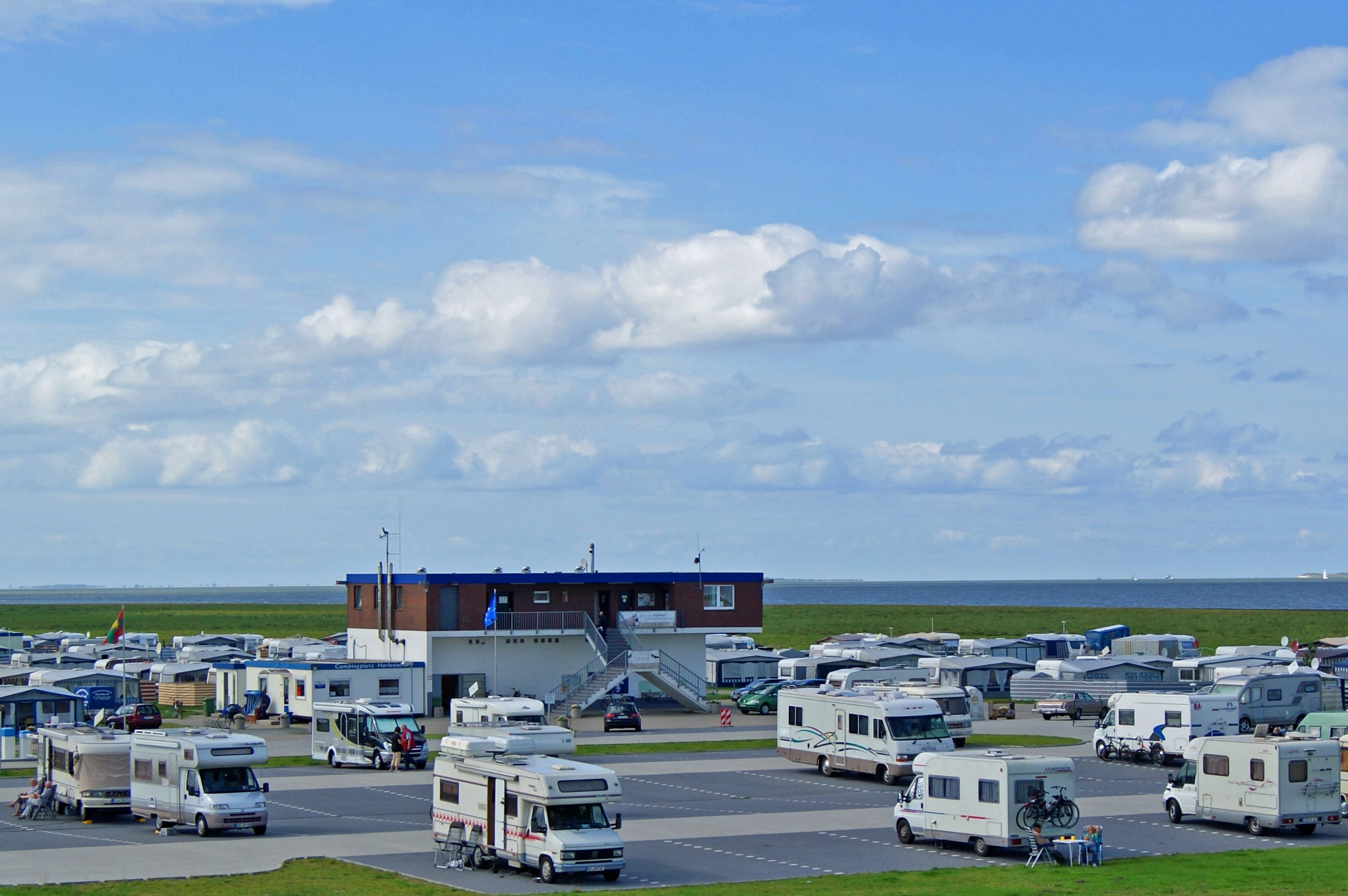 Campingplatz mit Wohnwagen und Wohnmobilen, Blick auf das Meer und ein Gebäude am Rand des Geländes.