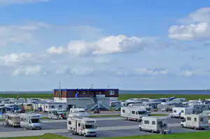 Campingplatz mit Wohnwagen und Wohnmobilen, Blick auf das Meer und ein Gebäude am Rand des Geländes.