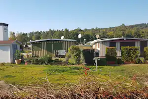Grüne Mobilheime auf einem Campingplatz mit gepflegtem Garten, Hecken, Töpfen und Rasen vor dem Gebäude.