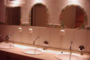 Camping-Badezimmer mit mehreren Waschbecken, Armaturen und Rundbogenfenstern in einer hell gefliesten Wand.