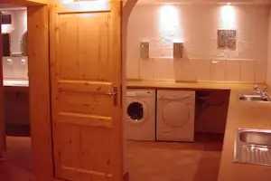 Holztür vor Küchenzeile im Campinghaus: Waschmaschine, Geschirrspüler, Spüle und Fliesenboden im Innenraum.